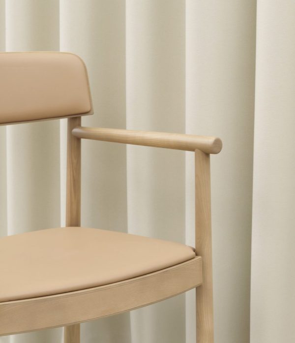 En minimalistisk stol med en beige læderpude og en træramme, sat på baggrund af lodrette creme- og hvidstribede gardiner, som eksemplificerer TomorrowsDesign.