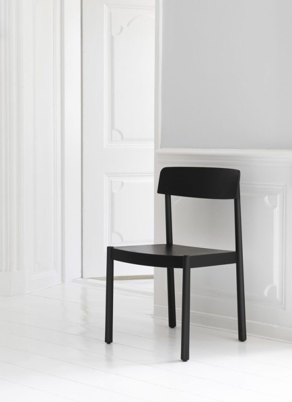 En minimalistisk sort stol placeret op ad en hvid væg med elegant støbning i et rum med hvidt trægulv, der afspejler sofistikeret interiørdesign.