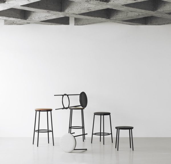 Fire moderne taburetter i varierende højder og design indrettet i et minimalistisk interiør med hvid væg og gråt betonloft. Et sfærisk hvidt tekstureret objekt fra TomorrowsDesign er på gulvet nær skamlerne.
