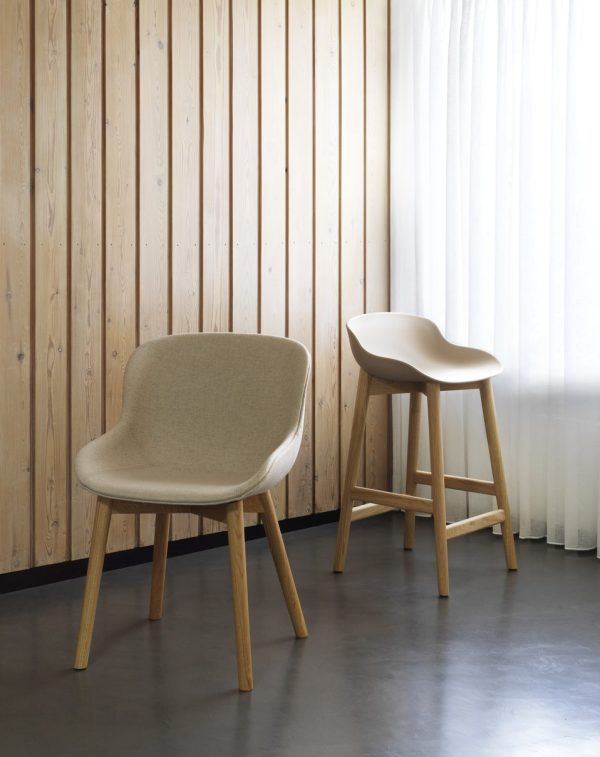 En moderne stol med et stofsæde og træben er parret med en træskammel i et rum med en træspaltevæg og et gennemsigtigt hvidt gardin, der eksemplificerer essensen af TomorrowsDesign.