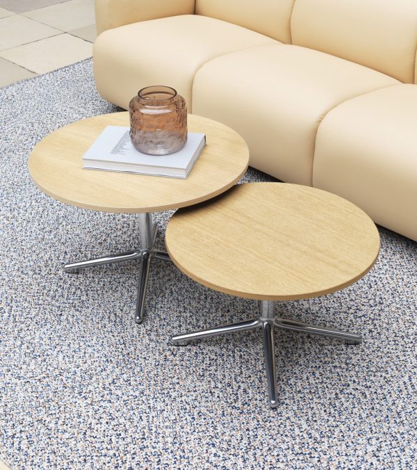 To små runde sideborde med træplader og metalben ved siden af en beige sofa. det ene bord rummer et lys i en glaskrukke og en bog, sat på NORMANN COPENHAGEN - Polli Gulvtæppe 170x240 tæppe.