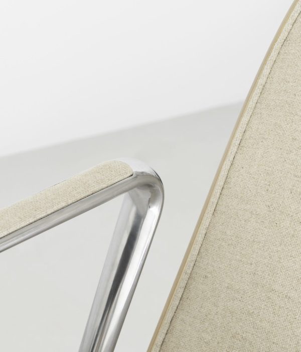 Nærbillede af en NORMANN COPENHAGEN - Pad Lænestol med en skinnende kromramme og lys beige stofbetræk, der fokuserer på den glatte kurve og led i armlænet.