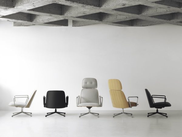 Fem NORMANN COPENHAGEN - Pad Lænestol stole i forskellige stilarter og farver, arrangeret på række på et betongulv mod en hvid væg med fritliggende loft over hovedet.