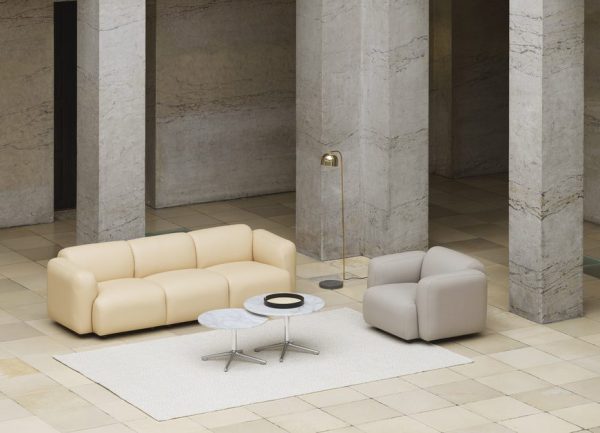 Et moderne opholdsrum med en beige sektionssofa og en matchende lænestol arrangeret på et hvidt tæppe med et NORMANN COPENHAGEN - Lunar Sofabord Ø70 i midten. Rummet har høje marmorsøjler og en gulvlampe.