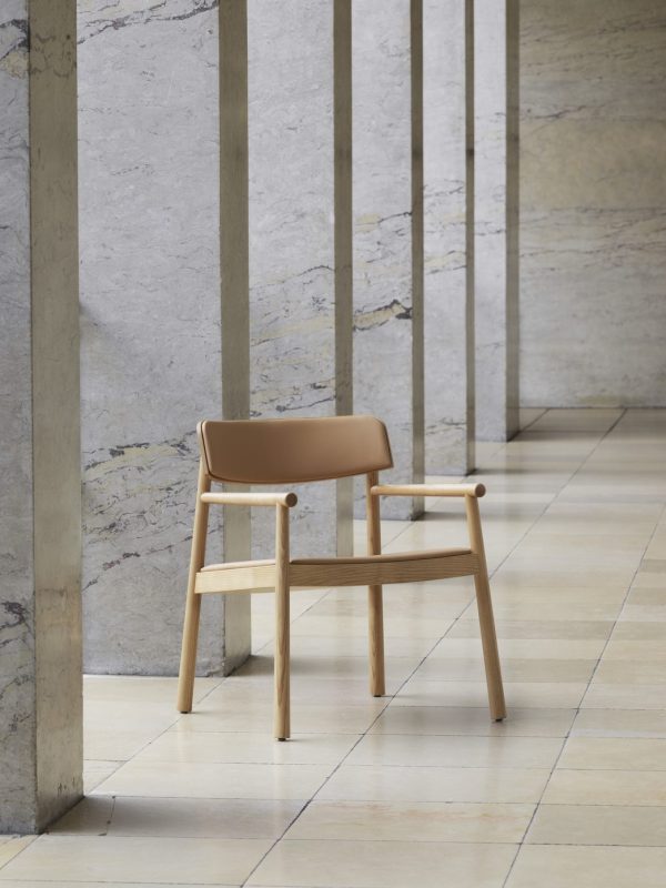 En moderne solbrun stol med træramme og arme, placeret i en korridor med polerede stengulve og jævnt fordelte lodrette søjler. Området har et minimalistisk og rent arkitektonisk design af TomorrowsDesign.
