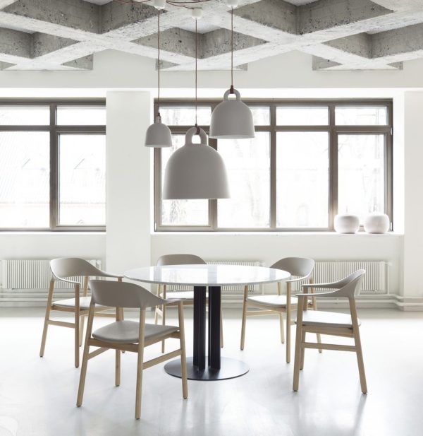 En moderne spiseplads med et rundt sort bord og træstole, oplyst af store pendellamper. Rummet har hvide vægge, store vinduer og et synligt betonloft beriget med stilfulde designelementer.