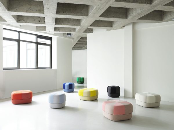 Et moderne, åbent rum med hvide vægge og synlige betonbjælker med en serie af NORMANN COPENHAGEN - Circus Puf Duo Stor-skamler arrangeret på tværs af gulvet nær store vinduer.