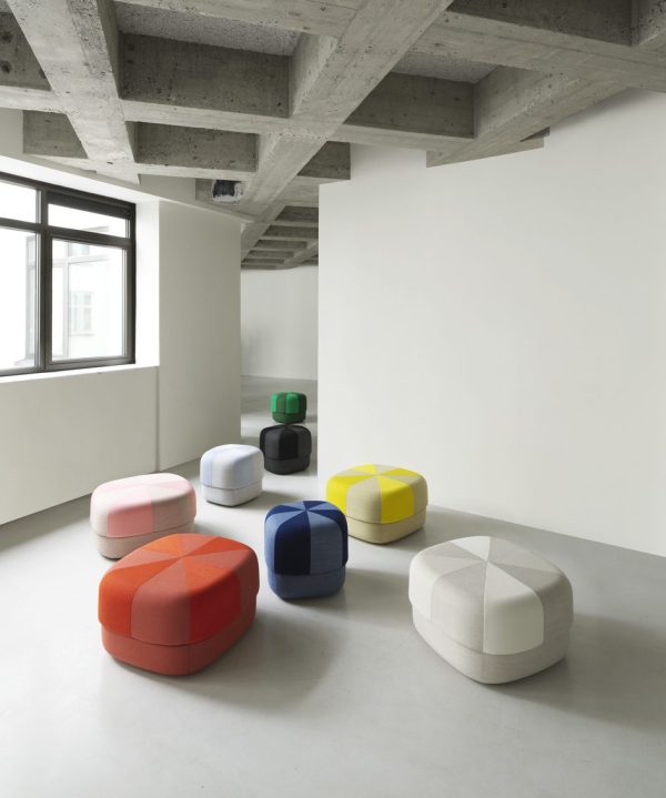 Et moderne, minimalistisk rum med synligt betonloft og hvide vægge, med en samling farverige, runde NORMANN COPENHAGEN - Circus Puf Duo Stor arrangeret i et velordnet mønster på et gråt gulv.