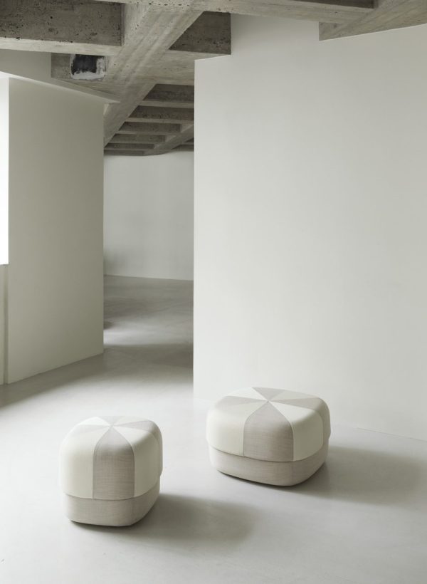 To moderne hvide ottomaner med tuftede toppe placeret på et gråt betongulv, sat i et kantet, minimalistisk hvidt rum med synlige betonloftsbjælker, der indbefatter TomorrowsDesign-æstetikken.