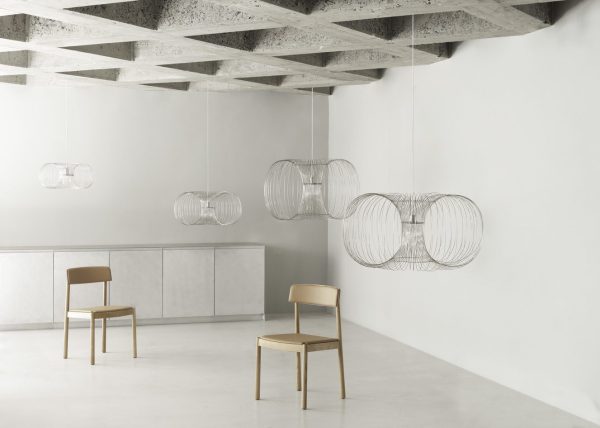 Et minimalistisk hvidt rum med et betonloft og hængende cirkulære wirependellamper inkarnerer et slankt design. Der er to træstole og et langt lavt skab langs den ene væg.
