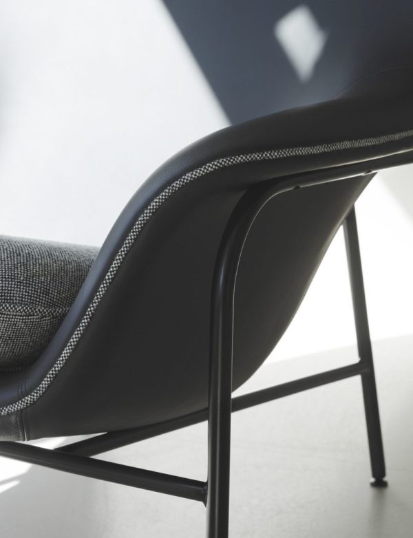Nærbillede af en moderne sort stol med et slankt design, der fremhæver dens teksturerede polstring og tynde metalben mod en blødt oplyst baggrund med skygger.