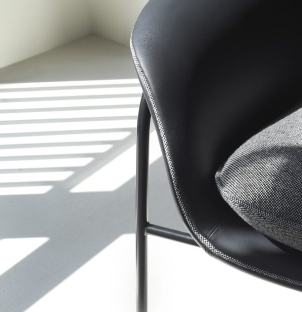 Sort moderne stol med en grå hynde i et lyst rum, der skaber geometriske skygger på det hvide gulv, som eksemplificerer essensen af TomorrowsDesign.