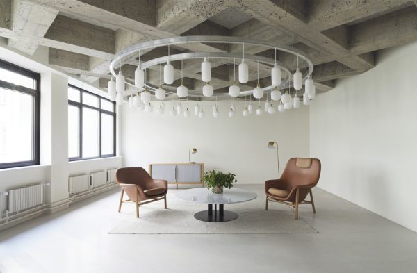 En moderne minimalistisk stue med to solbrune læderstole, et rundt sofabord og en udførlig cirkulær hvid lysekrone. Rummet har store vinduer og synlige betonlofter. Nyd essensen af TomorrowsDesign i alle detaljer i dette interiør.