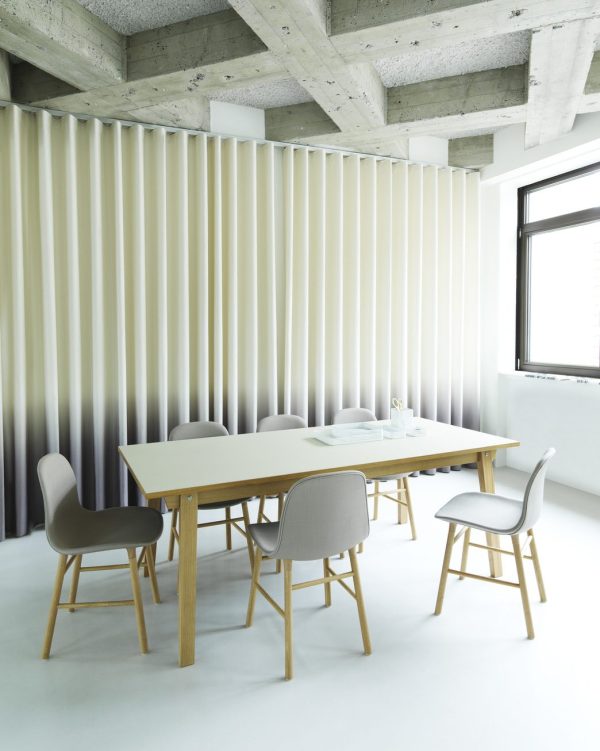 Et moderne kontorrum designet af TomorrowsDesign, med et langt træbord og fire grå stole på et hvidt gulv, med lodrette ribbede gardiner og et synligt betonloft. Et vindue giver naturligt lys til rummet.