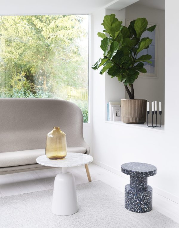 Et minimalistisk stuehjørne med en beige sofa, et marmorsofabord med en gul glasvase, to NORMANN COPENHAGEN - Bit Skammel taburetter og en stor violinfigen i potte ved et vindue.