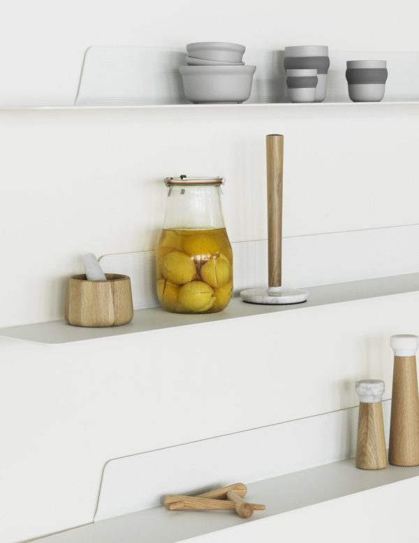 En moderne køkkenhylde med en NORMANN COPENHAGEN - Craft Køkkenrulleholder, en krukke med konserverede citroner, små skåle og diverse køkkenredskaber. Indretningen er minimalistisk med hvid baggrund.
