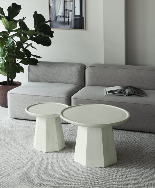 Moderne stue med en grå sektionssofa med to NORMANN COPENHAGEN - Pine Sofabord Ø45 foran og en frodig potteplante ved siden af. et magasin er åbent på det ene bord, og et abstrakt kunstværk hænger på væggen.