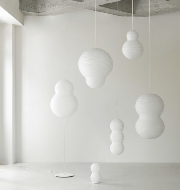 Minimalistisk interiør med forskellige hvide, skulpturelle pendellamper ophængt i et betonloft, suppleret med en NORMANN COPENHAGEN - Puff Lampe Twist gulvlampe i et lyst, luftigt rum.