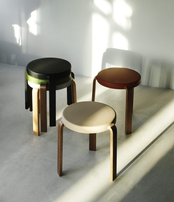 Tre NORMANN COPENHAGEN - Tap Skammel taburetter med forskellige farvede toppe - sort, brun og creme - er arrangeret på et betongulv i et soloplyst rum og kaster bløde skygger på jorden.