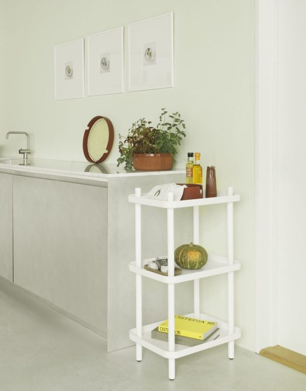 Et minimalistisk køkkenhjørne, der viser en hvid, tre-lags NORMANN COPENHAGEN - Block Reol med forskellige ting, herunder et græskar og bøger. ovenover ses en grå bordplade med vask og potteplanter, mod en lysegrøn væg med indrammet kunst.