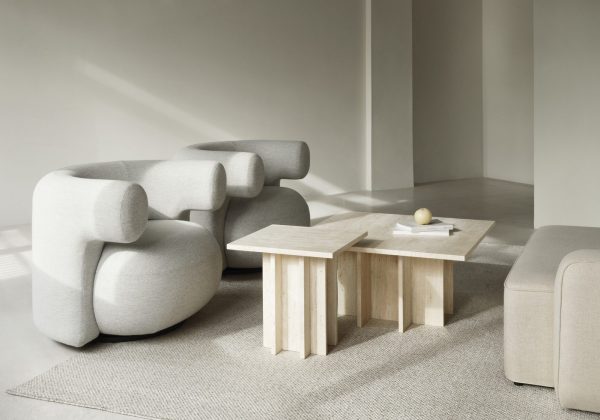 Minimalistisk stue med skulpturelle lysegrå sofaer, et sofabord af træblokke og beige tæppe under naturlig belysning, hvilket skaber en rolig atmosfære med elegant designmøbler.