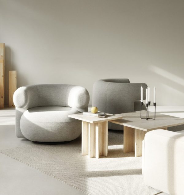 En minimalistisk stue med en blød grå lænestol, en matchende sofa og et sofabord i træ. Stearinlys og en lille gul genstand står på bordet, alt sammen oven på et tekstureret tæppe i et blødt oplyst rum fyldt med TomorrowsDesign-møbler.
