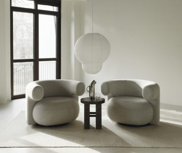 To moderne, grå polstrede lænestole over for hinanden med et lille sort bord imellem, sat på et beige tæppe i et minimalistisk rum med et stort vindue og en hvid, kugleformet pendel og NORMANN COPENHAGEN - Fyr Skammel.