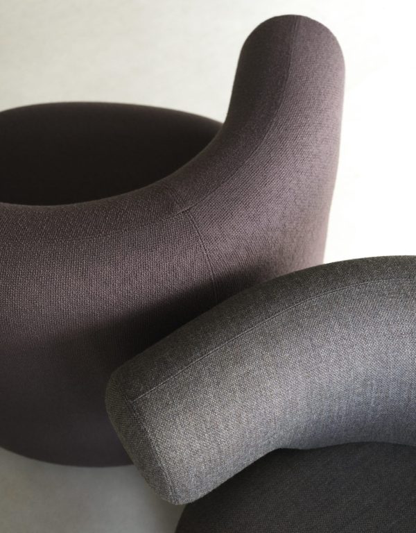 Nærbillede af to NORMANN COPENHAGEN - Burra Loungestol M. Drejefunktion med tekstureret gråt polstring. forgrundsstolen har et unikt afrundet ryglæn, mens stolen i baggrunden viser et buet armlæn.