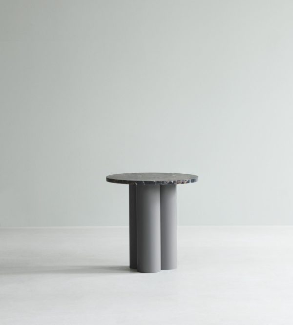 Et moderne, minimalistisk sidebord med en cylindrisk sort bund og en cirkulær, ru tekstureret mørkegrå plade, sat mod en almindelig lysegrå kulisse af NORMANN COPENHAGEN - Dit Bord.