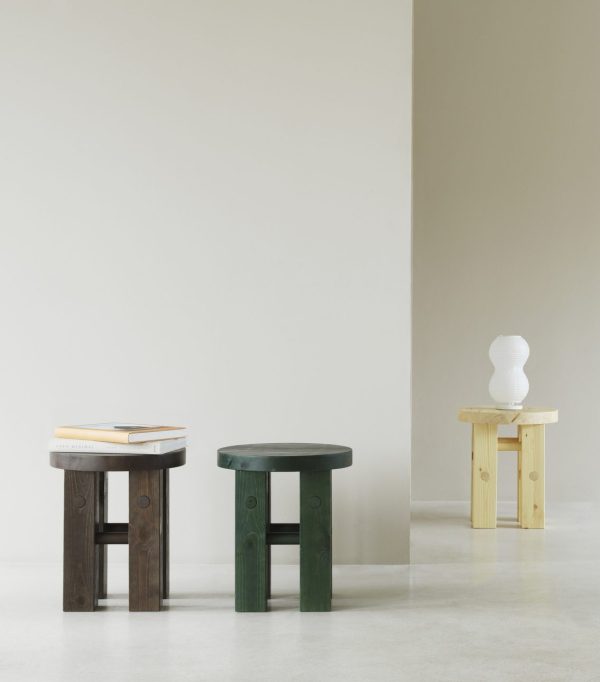 Tre NORMANN COPENHAGEN - Fyr Skammel med varierende højder og farver er arrangeret mod en neutral baggrund - den første mørk med bøger, den anden almindelig grøn, den tredje understøtter en hvid vase.