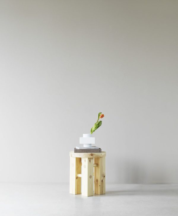 En minimalistisk indstilling med en NORMANN COPENHAGEN - Deko Object S4, der understøtter en stak bøger, toppet med en hvid platform, der holder en enkelt tulipan. Baggrunden er almindelig og lysfarvet.