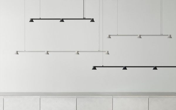 Et minimalistisk køkkeninteriør med en grå betonbordplade og tre forskudte svævende hylder med et slankt, moderne design mod en ren hvid væg og NORMANN COPENHAGEN - Hat Lampe Linear L115.