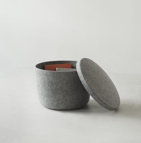 En rund, grå NORMANN COPENHAGEN Hide Opbevaringspuf Stor med åbent låg, afslørende bøger indeni, placeret på en lysegrå baggrund.