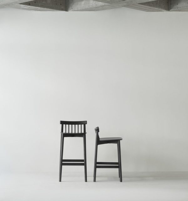 En minimalistisk indstilling med en enkelt sort stol med et højt ryglæn, der understreger slankt design, placeret mod en almindelig hvid væg i et rum med betonloft.