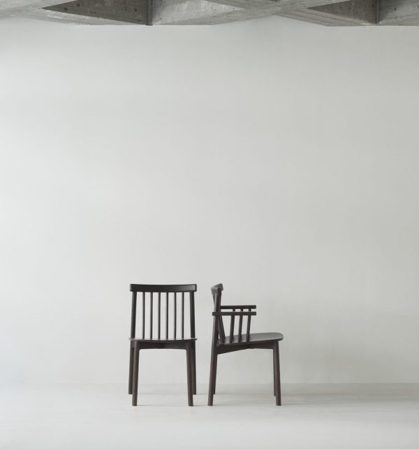 To mørke træstole står op ad en almindelig hvid væg i et minimalistisk, veloplyst interiør med synlige betonloftsbjælker.