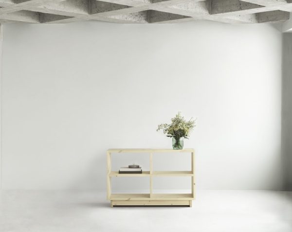 Et minimalistisk værelse med en NORMANN COPENHAGEN - Plank Bogreol Mellem med en lille stak bøger, en dekorativ vase med grønt og en lille grå genstand, sat op mod et betonloft og en almindelig hvid væg.