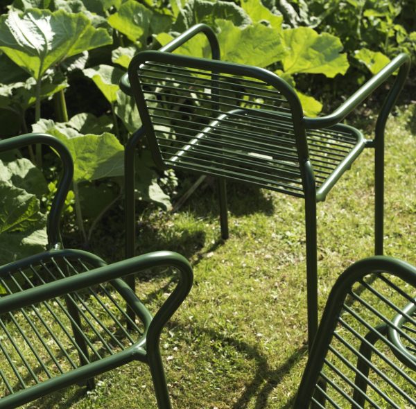 Grønne NORMANN COPENHAGEN - Vig Havestol stole opstillet på et græsareal, omgivet af store bladplanter, med sollys, der kaster skygger på jorden.