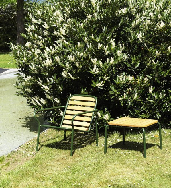 EN NORMANN COPENHAGEN - Vig Bord 55X45 med vedhæftet lille gult bord, placeret på græs ved siden af en blomstrende busk med hvide blomster, under sollys.