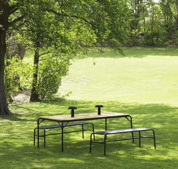 EN NORMANN KØBENHAVN - Vig Bænk og to bænke i en frodig grøn park, omgivet af træer og en pænt slået græsplæne, der formidler en fredelig udendørs ramme.