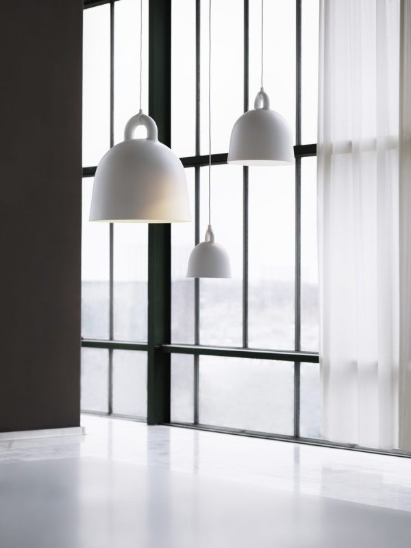 Tre NORMANN COPENHAGEN Bell Lampe Ø22 hænger i forskellige højder i et moderne rum med store vinduespartier med udsigt over en lys, vag baggrund, spredt af rene gardiner. scenen formidler en minimalistisk og rolig stemning.