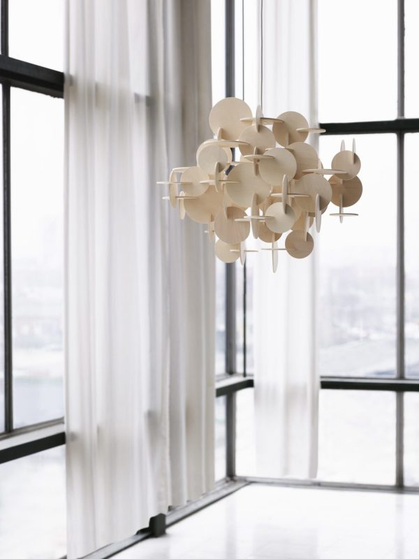 EN NORMANN KØBENHAVN - Bau Lampe hænger i et lyst rum med store glasvinduer og blanke hvide gardiner, med udsigt over et bybillede. Det luftige og minimalistiske rum understreger rene linjer og lys.