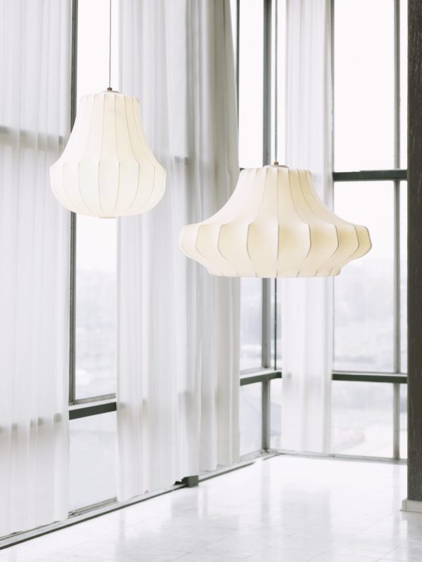 To NORMANN COPENHAGEN - Phantom Lampe Mellem hænger elegant foran et stort vindue med rene hvide gardiner, med udsigt over et lyst, sløret bybillede.