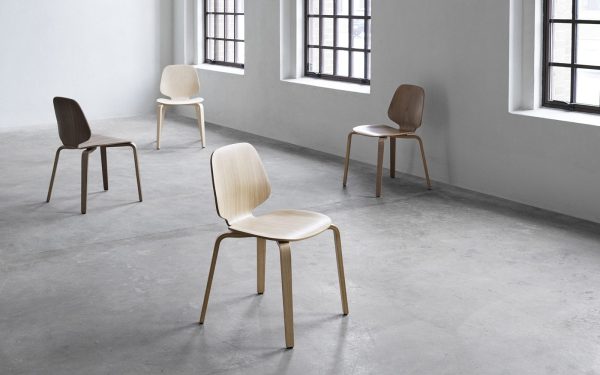 Fire moderne stole i forskellige nuancer fordelt på et betongulv i et minimalistisk rum med hvide vægge og flere vinduer, som viser eksemplarisk interiørdesign.
