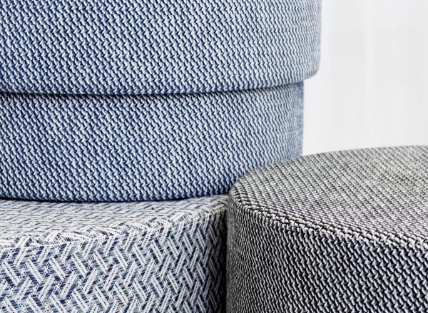 Nærbillede af tre stablede NORMANN COPENHAGEN - Silo Puf Medium med tekstureret vævet stof i forskellige nuancer af grå og blå. fokus er på de detaljerede mønstre og stofteksturer.