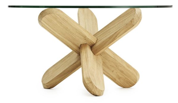 NORMANN COPENHAGEN - Ding Sofabord Ø75 med en klar glasplade og en unik base lavet af sammenlåsende træbjælker i en naturlig finish. Basens design ligner en tredimensionel x-form.
