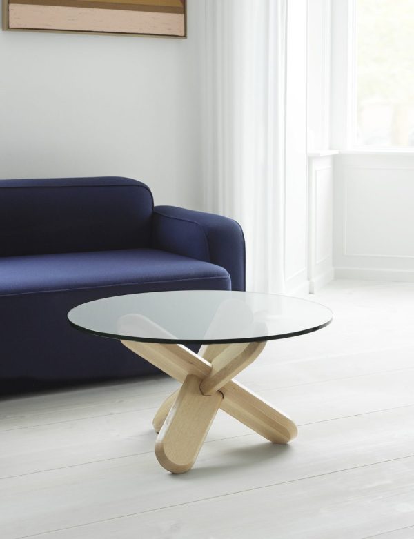 En moderne stue med NORMANN COPENHAGEN - Ding Sofabord Ø75 og et rundt sofabord med glasplade med en unik træbund. rummet har hvide vægge og lyst trægulv, med naturligt lys fra et vindue.