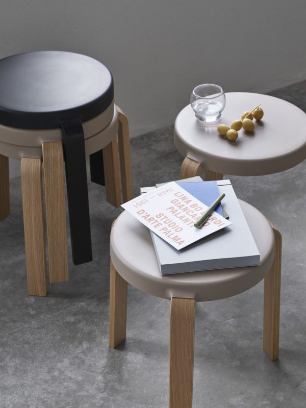 Tre NORMANN COPENHAGEN - Tap Skammel taburetter med runde polstrede toppe og træben i et rum, en med bøger, en anden med et glas vand og dekorative perler.