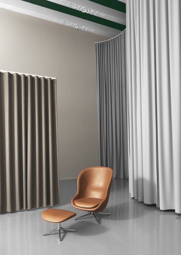 Et moderne, minimalistisk interiør med en stilfuld NORMANN COPENHAGEN - Hyg Swivel Fodskammel med en matchende skammel, sat på baggrund af grå og draperede gardiner i et rum med dekorativ kroneliste og varierende teksturer på væggene.