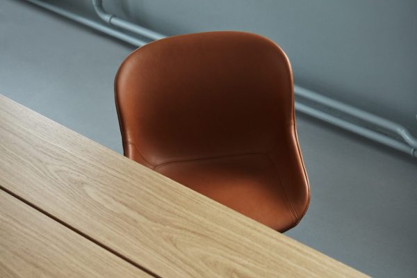 En brun moderne stol med en kurvet designmøbler, placeret ved siden af et træbord i et værelse med gråt gulv.