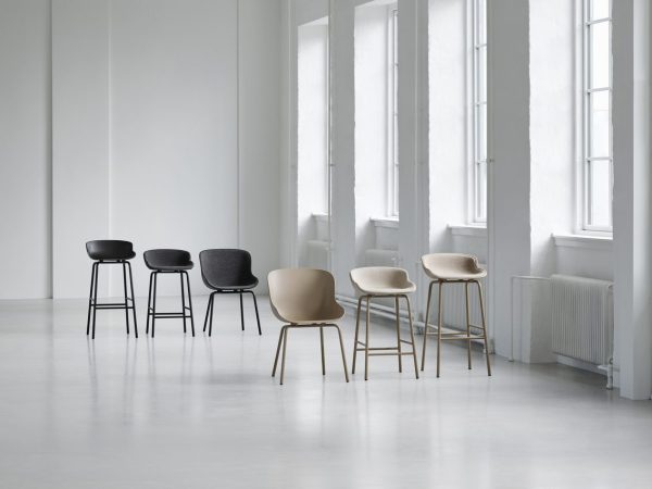 Fire moderne design barstole med varierende design og farver, arrangeret i en linje på et lækkert, hvidt gulv i et lyst rum med store vinduer og hvide vægge.